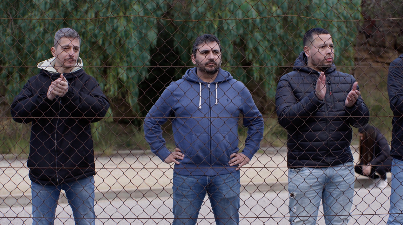 Tres adultos siguen un partido detrás de la valla del campo.