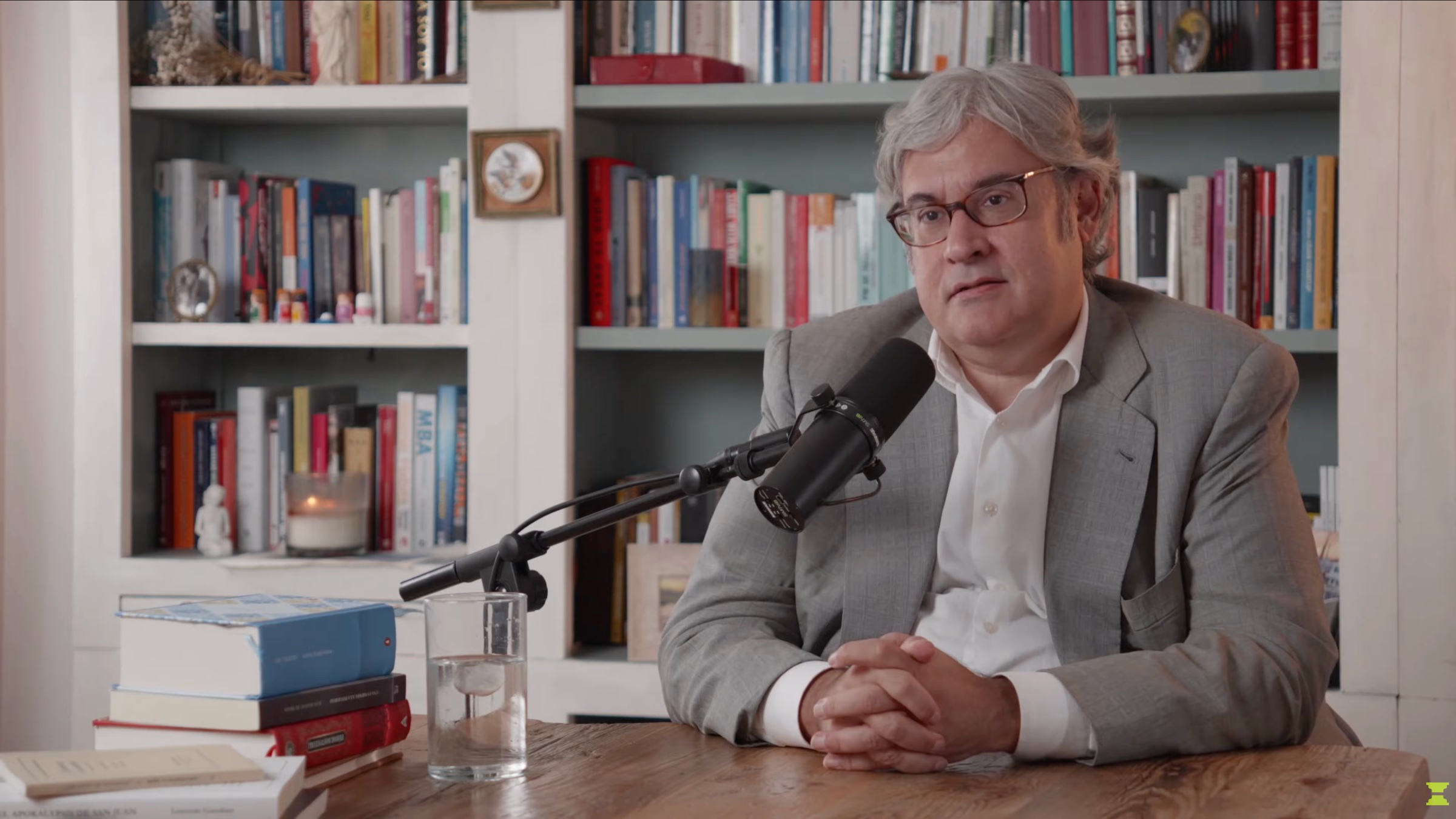 Un participante de Thenomba conversa ante un micrófono, con una biblioteca al fondo.