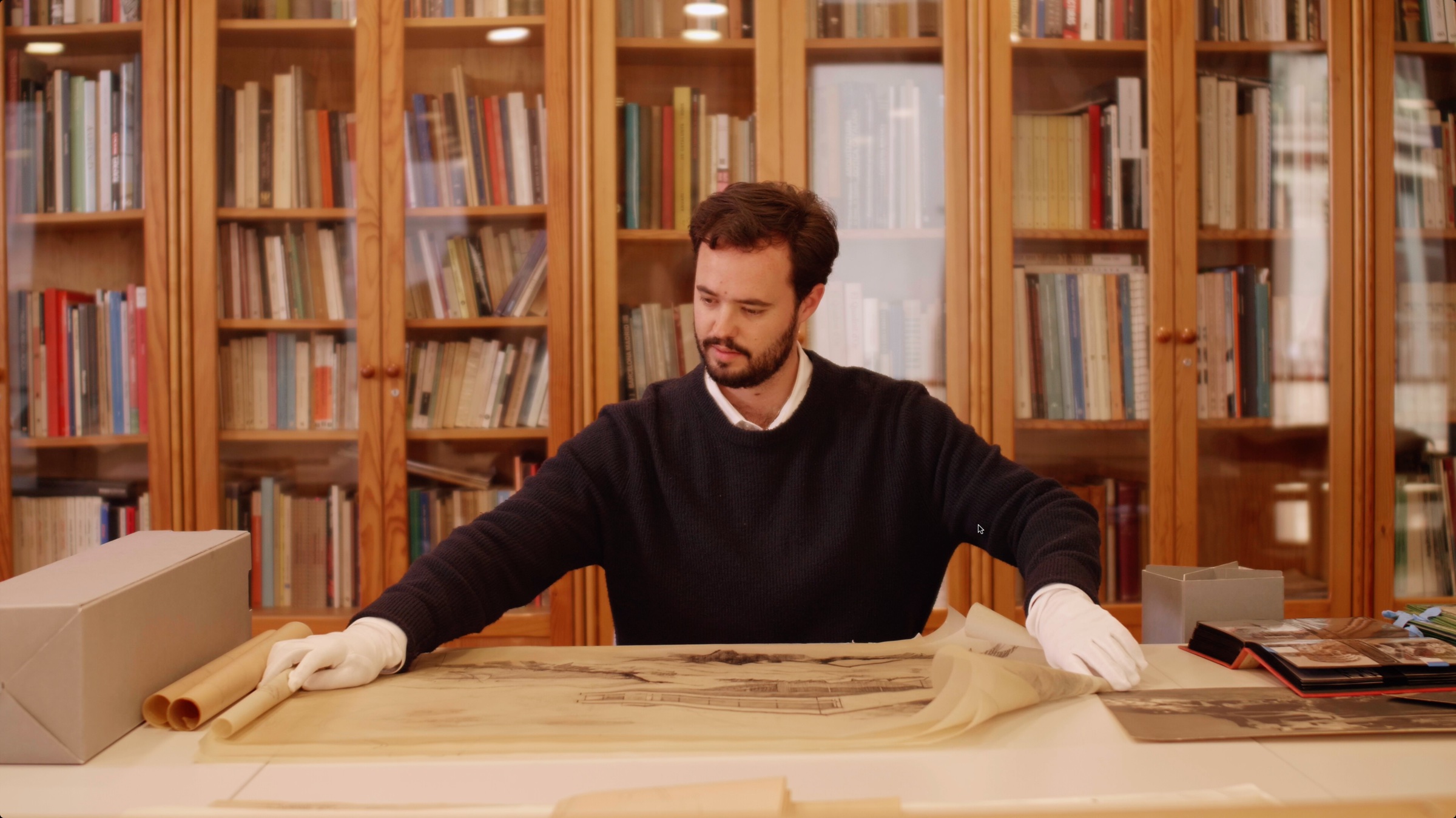 Consulta de planos de archivo con guantes, en una biblioteca, en una escena del documental.